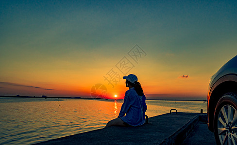 日落时分 孤独的年轻女子戴着一顶帽子 独自在车前的海滩上放松 天空是橙色和蓝色的 暑假和旅行的概念太阳自由运动海滨海岸幸福女士热图片