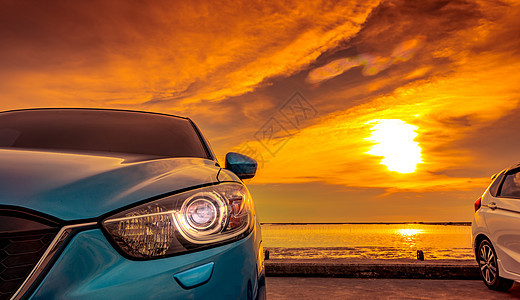蓝色和白色的紧凑型 SUV 汽车 具有运动和现代设计 日落时分停在海边的水泥路上 环保技术 商业成功理念 打开头灯灯的汽车背景图片