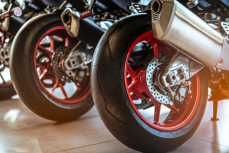 新的摩托车后轮特写镜头 大自行车停在经销店陈列室里 摩托车排气管 具有运动设计的标志性摩托车 带有独特花纹的黑色轮胎和红色辐条轮图片