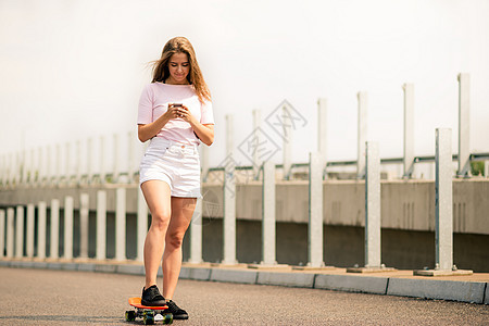 在滑板上使用智能手机的 年轻美丽的微笑女孩图片