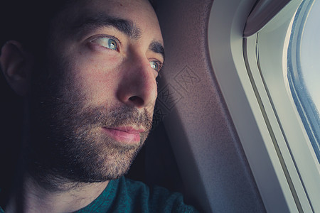 近距离靠近一个从窗外向外看的笔记人沉思运输成人喷射男人航班微笑情绪化戏剧性低角度图片