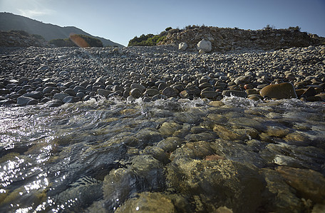 卵石海滩上的海水蓝色鹅卵石海岸线海岸苦瓜海景天空太阳场景石头图片