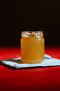 玻璃罐中的蜂蜜紧靠在红色木桌上的黑色背景上 用棒状蜂蜜勺倒蜂蜜液体早餐作品男人厨房梳子营养橙子玻璃生物图片