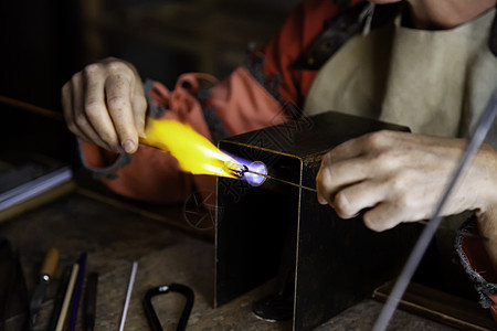 以传统方式吹着玻璃鼓风机作坊管子材料火焰制作者辉光艺术家生产手工图片