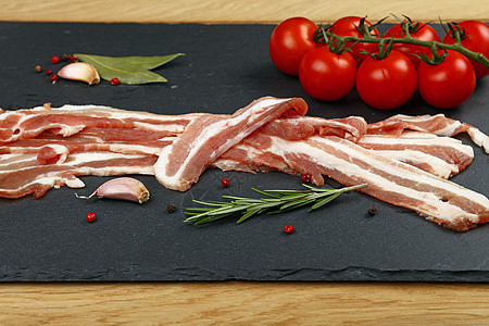 黑板上的生培根切片 香料和番茄迷迭香早餐烹饪营养猪肉黑色美食树叶石板调味品图片