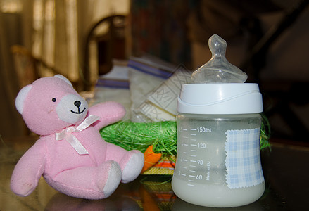 背景中婴儿奶瓶中新鲜挤出的母乳 粉色泰迪熊和储物袋中的冷冻母乳图片