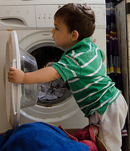 一岁半男婴把衣服放进洗衣机家务器具女士父母房子婴儿危险白色洗衣店推杆图片