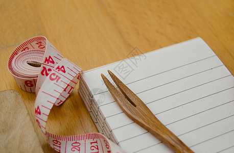 木桌上用木叉和测量胶带装在木板上的笔记本笔记本食物美食烹饪记事本木头棕色桌子菜单白色食谱图片