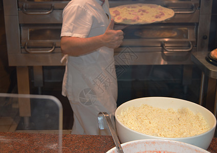 穿白色围裙的厨师做一个大披萨 特写了比萨配料火 芝士 黑暗背景食物面团烹饪巡航糖果桌子男性美食餐厅厨房图片
