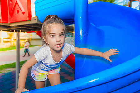 可爱小女孩在滑板上攀爬的肖像童年女孩蓝色公园孩子女性玩具喜悦塑料操场图片