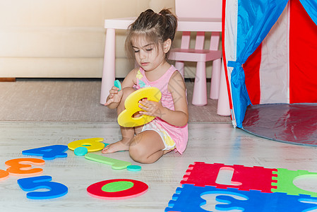 小女孩坐着 拿着多彩的拼谜游戏垫子学习橡皮乐趣玩具女孩闲暇托儿所孩子数字拼图图片