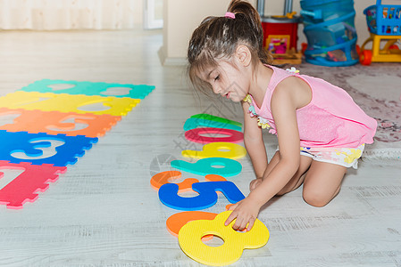 小女孩坐着 拿着多彩的拼谜游戏垫子幼儿园数字童年地毯泡沫女孩地面拼图闲暇教育图片