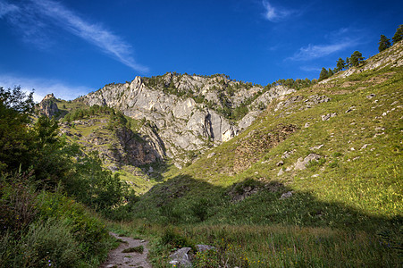 在山之间 有一条狭窄的道路 它覆盖青绿的旅游海滩山脉风景森林全景蓝色岩石爬坡绿色图片