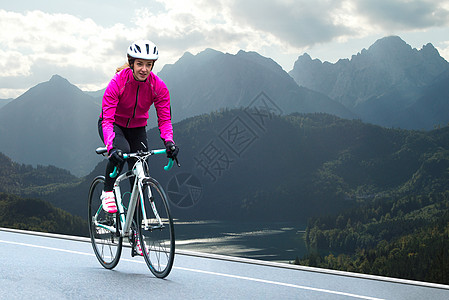 在高山路上的闪亮粉红夹克骑行路双轮赛中年轻女子 健康生活方式和冒险概念头盔活动速度自由爱好女性竞赛女孩自行车运动图片