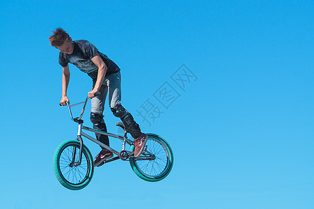 年轻的BMX摩托车手 脚在BMX上保护双腿 在背景天空上玩空气把戏图片