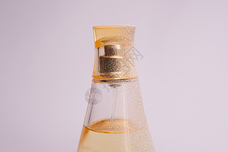 暖黄色玻璃香水瓶 白色紫色背景上有人造雪 特写视图芳香化妆品香味水彩优雅反射女性金子香气喷雾器背景图片