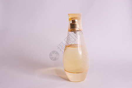 暖黄色玻璃香水瓶 白色紫色背景上有人造雪 特写视图优雅奢华喷雾器香水香气金子卫生水彩液体女性背景图片