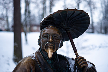 冬雪公园一个带雨伞的中国老人的铜质纪念碑 其背景模糊而封闭哲学家艺术石头文化历史青铜历史性旅行建筑学寺庙图片