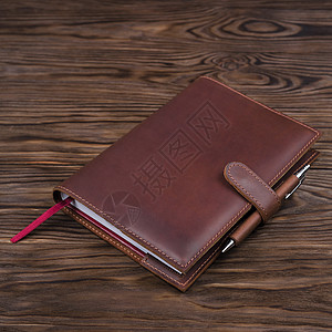 红色手工制作的皮革笔记本封面 有笔记本和笔印在木制背景上 奢侈商业配件的库存照片图片