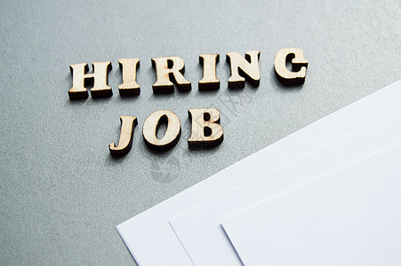 hiringHiring JOB 是用木制字母写在灰色背景上的 靠近白纸布局 用于设计布局招聘概念面试广告笔记公司工作工人办公室失业雇主插图背景