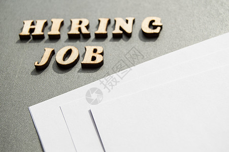 hiringHiring JOB 是用木制字母写在灰色背景上的 靠近白纸布局 用于设计布局招聘概念帮助职员插图笔记工人办公室写作面试失业就业背景