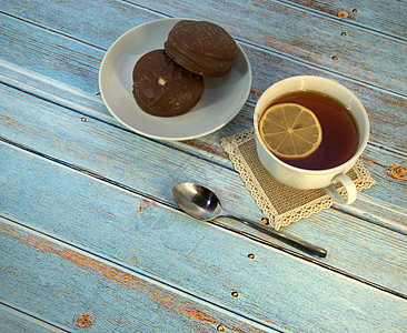 木桌上放着一杯茶和柠檬勺 盘子上放着两块巧克力蛋糕柠檬勺子桌子糕点巧克力甜点菜肴早餐美食液体图片