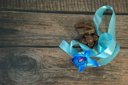 一盒巧克力 蓝色丝带 蓝色兰花花蕾和木桌上的装饰球木头惊喜生日盒子风格包装礼物念日桌子庆典图片