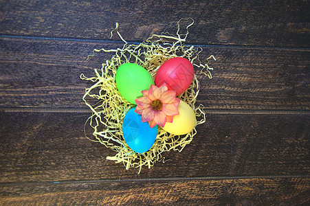 四个漆成复活节的鸡蛋在稻草巢中 中间有花朵 躺在木制桌子上手工传统庆典团体材料风格产品装饰季节蓝色图片