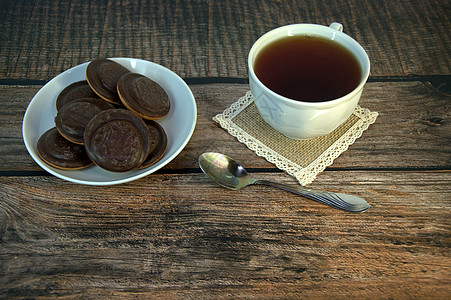 木桌上放着早餐 一杯茶和饼干 瓷杯和勺子上放着巧克力糖霜饮食茶匙食物作品营养杯子桌子液体盘子红茶图片