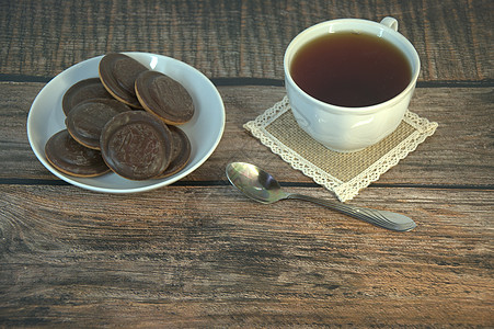 木桌上放着早餐 一杯茶和饼干 瓷杯和勺子上放着巧克力糖霜糖果茶匙盘子海报营养作品液体食物饮食桌子图片