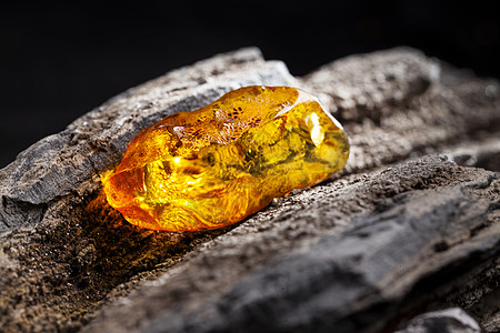天然琥珀 黄色透明的天然琥珀 在大片黑石头木头的一块上珠子蜂蜜宏观矿物琥珀色抛光反射珠宝材料烙印图片