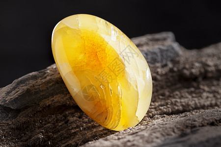 天然琥珀 黄色不透明的天然琥珀 在大片黑石头木头上抛光矿物反射珠宝珠子化石太阳石裂缝宏观蜂蜜图片