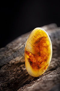 天然琥珀 黄色不透明的天然琥珀 在大片黑石头木头上材料反射矿物太阳石裂缝琥珀色化石黄油珠宝珠子图片