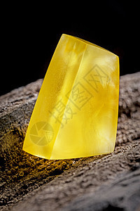 天然琥珀 黄色不透明的天然琥珀 在大片黑石头木头上太阳石裂缝宝石蜂蜜琥珀色分层黄油矿物化石宏观背景图片