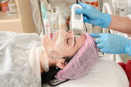 在美容院的年轻女子 做超声波剥皮 和面部清洗程序护理药品刺激医生美容师温泉电疗电泳真空收音机图片