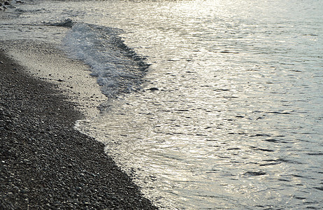 清晨日出海卵石海滩上闪亮的银色水卵石海浪支撑岩石阳光蓝色反射海洋泡沫海岸图片