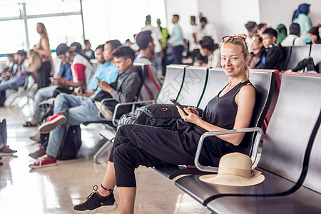 女性旅行者在等待登上Asian机场终点站出入口的飞机时 使用手机进行旅行地球航班运输太阳镜空气女孩车站耳机游客旅游图片
