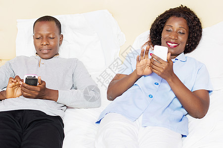 在床上操纵手机的年轻夫妇在床上笑着微笑图片