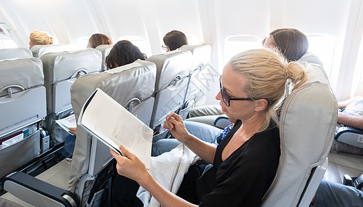 飞行期间在飞机上看 女性 杂志 女旅行者坐在过客舱里阅读航空公司商业窗户旅行娱乐报纸女士航班游客女孩图片