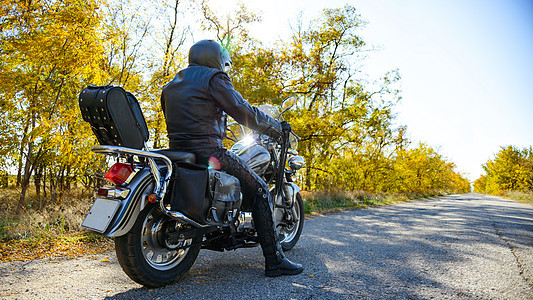 摩托车驾驶员在秋天路上乘坐自定的自行车 旅行和冒险概念图片