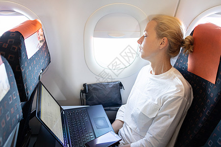 女商务人士在她出差时 在飞机上睡午觉的疲劳妇女航班旅游木板休息小憩喷射手臂座位蓝色商业背景