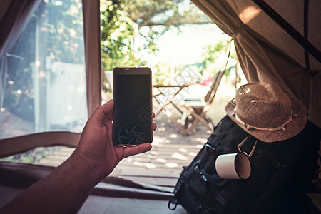 一个在露营帐篷里拿着电话的男人的手旅行家庭太阳娱乐背包闲暇成人手臂视角远足图片