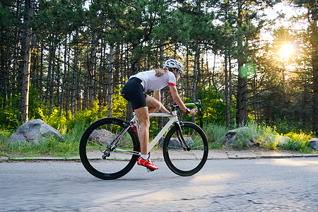 骑自行车女青年女赛车手骑着路自行车在夏日热火的森林中走免费道路 健康生活方式概念活动森林女孩成人头盔运动冒险公园街道自由背景