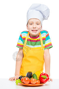 男孩在厨师的帽子和围裙上 用一盘蔬菜隔离图片