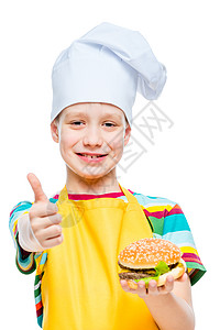 快乐的男孩以帽子和围裙做饭 用芝士汉堡和小菜图片