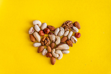 各种坚果在黄色背景上以心形排列 平躺 从上面看 复制空间 医疗保健 有氧运动 适当营养 健康脂肪的概念图片