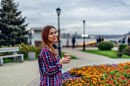 美丽的年轻女子拿着咖啡杯 在公园笑着微笑杯子女性快乐食物衬衫咖啡头发金发女郎日落女士图片
