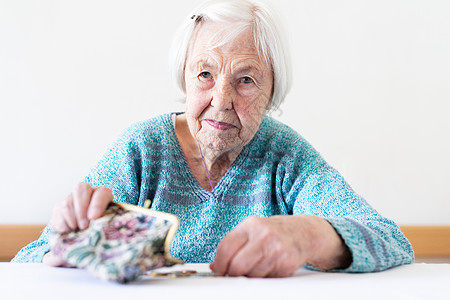 坐在桌边的关心她的老年妇女在钱包里数钱 笑声皮革孤独女士女性债务退休贫困账单情感金融图片