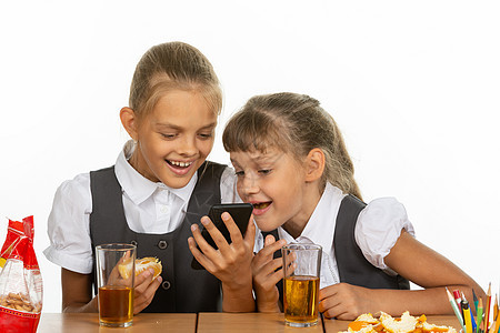 两个女学生在休息时间 观看一个视频 在电话上 吃肝和橙子 喝果汁图片