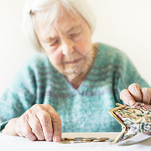 坐在桌边的关心她的老年妇女在钱包里数钱 笑声女性退休贫困生存硬币商业孤独成人皮革债务图片